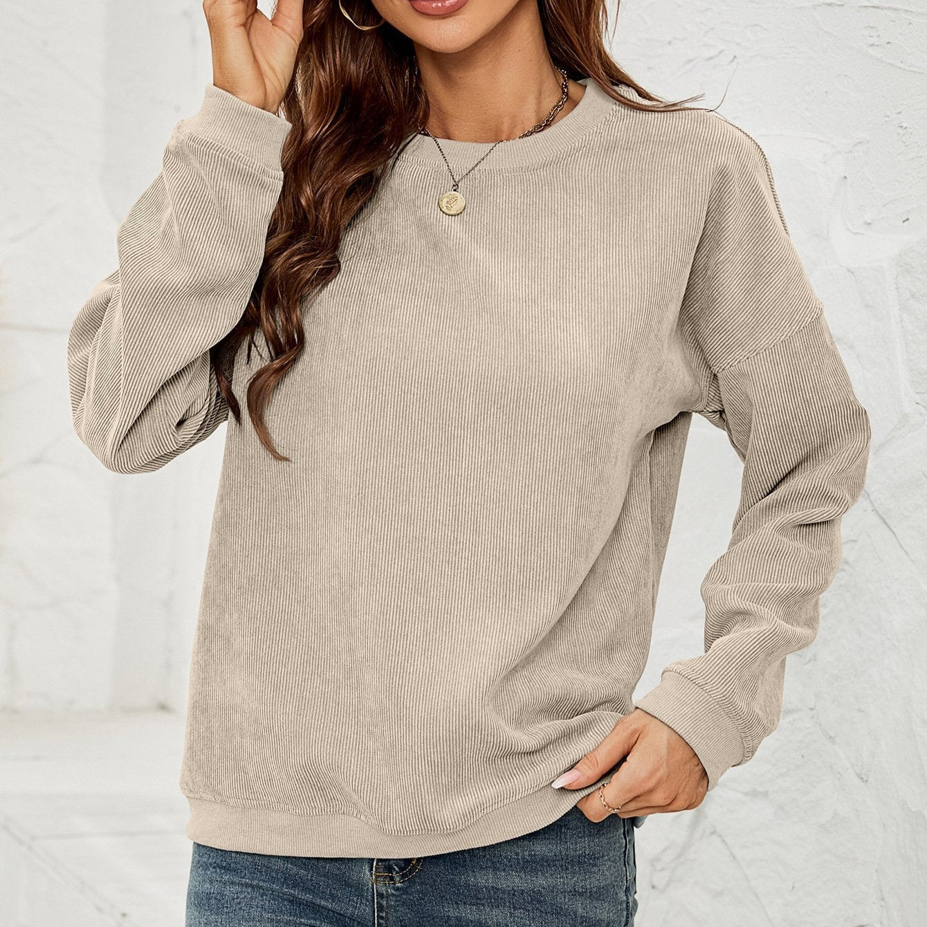 Frau in beigem Cordpullover, lässig gestylt mit blauen Jeans. Modetrend Herbst, gemütlicher Look, Damenmode, Freizeitkleidung.