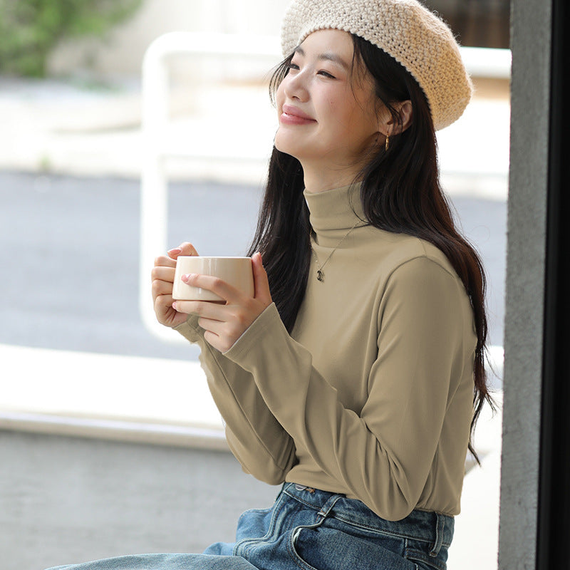 Frau mit beigem Rollkragenpullover und Strickmütze hält Tasse Kaffee, sitzt lächelnd draußen. Herbstmode, Entspannung, Kaffeegenuss.