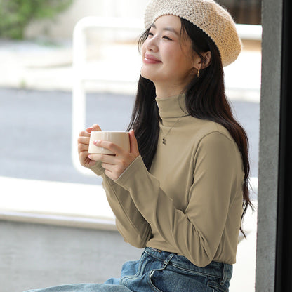 Frau mit beigem Rollkragenpullover und Strickmütze hält Tasse Kaffee, sitzt lächelnd draußen. Herbstmode, Entspannung, Kaffeegenuss.