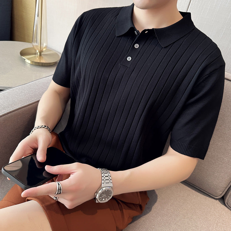 Person in schwarzem Polohemd mit Smartphone in der Hand, sitzt auf einem Sofa. Armbanduhr und Armband sichtbar. Moderne, lässige Herrenmode.