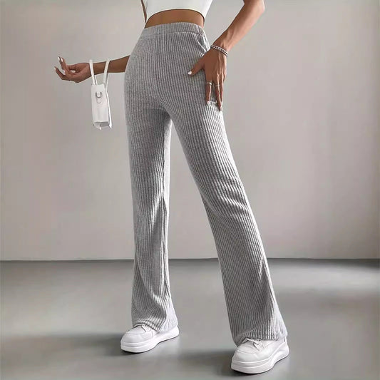 Frau in grauer, gerippter Schlaghose und weißem Crop-Top, hält kleine weiße Handtasche, trägt weiße Sneaker. Modetrend, Damenbekleidung, Streetstyle.