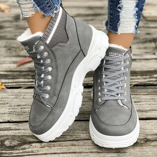 Graue Damen-Sneaker mit dicker Sohle, getragen mit zerrissenen Jeans auf Holzuntergrund. Modische Herbstschuhe, bequem und stilvoll.