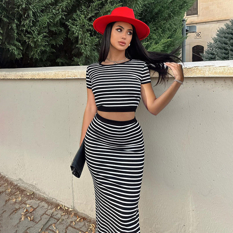 Frau in schwarz-weiß gestreiftem Kleid und rotem Hut lehnt an einer Mauer, modisches Outfit, Sommermode, stilvolle Kleidung, Outdoor-Fotografie.