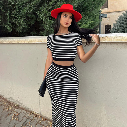 Frau in schwarz-weiß gestreiftem Kleid und rotem Hut lehnt an einer Mauer, modisches Outfit, Sommermode, stilvolle Kleidung, Outdoor-Fotografie.