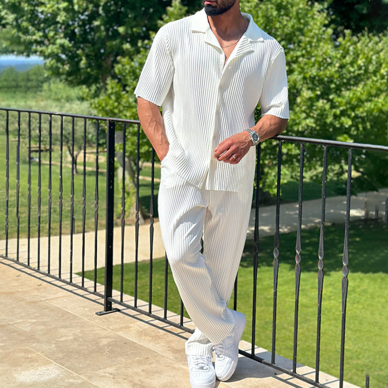 Mann in weißem, gestreiftem Sommeranzug lehnt lässig an einem Geländer im Freien. Stilvolle Herrenmode, Freizeitlook, Sommeroutfit.