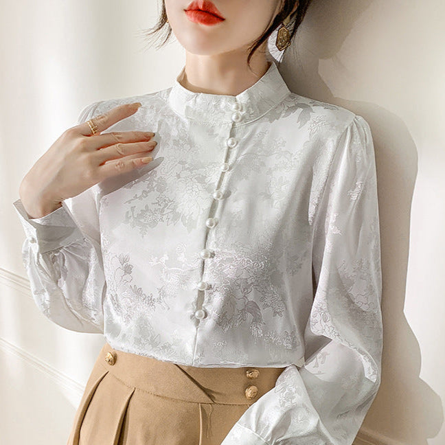 Frau in eleganter weißer Bluse mit floralen Mustern und Stehkragen, kombiniert mit beiger Hose. Modetrend, Damenmode, stilvolle Kleidung.