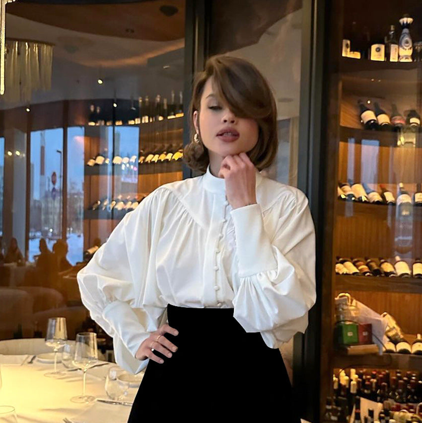 Eine Frau in eleganter weißer Bluse steht vor einem Weinkeller in einem Restaurant. Sie trägt einen schwarzen Rock und posiert selbstbewusst.