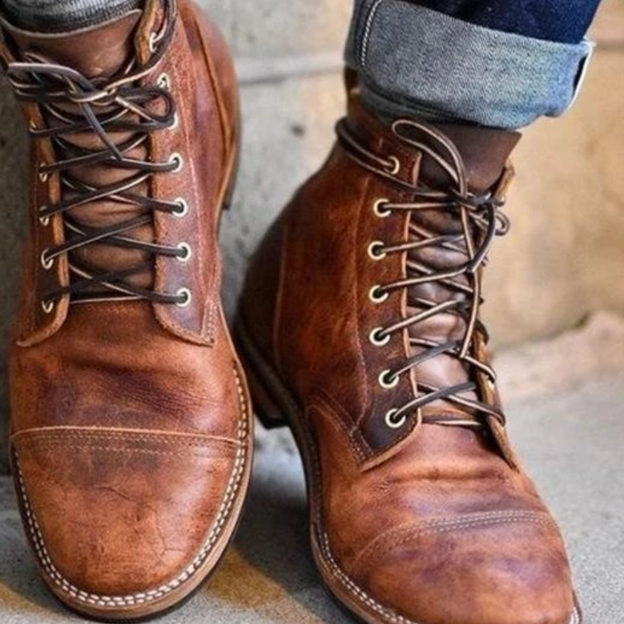 Braune Lederstiefel mit Schnürung, getragen von Person mit hochgekrempelten Jeans. Robuste, stilvolle Herrenstiefel für Herbstmode.