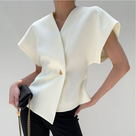 Elegante Frau in weißer, ärmelloser Bluse mit goldener Brosche, hält schwarze Handtasche mit Kettendetail. Mode, Damenbekleidung, Stil.