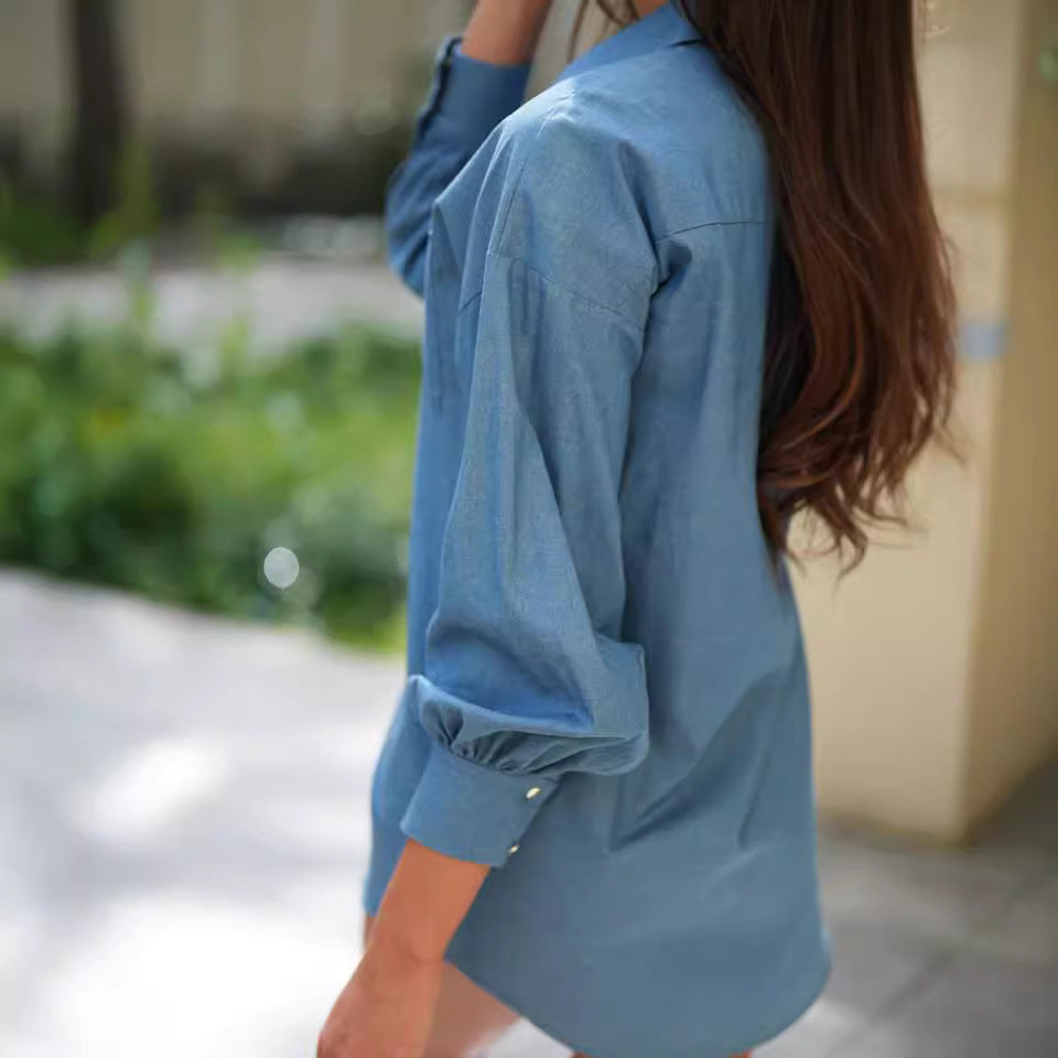 Frau in blauem Hemd mit langen Ärmeln, im Freien, Rückenansicht. Langes braunes Haar, lässiger Stil, sommerliche Umgebung.