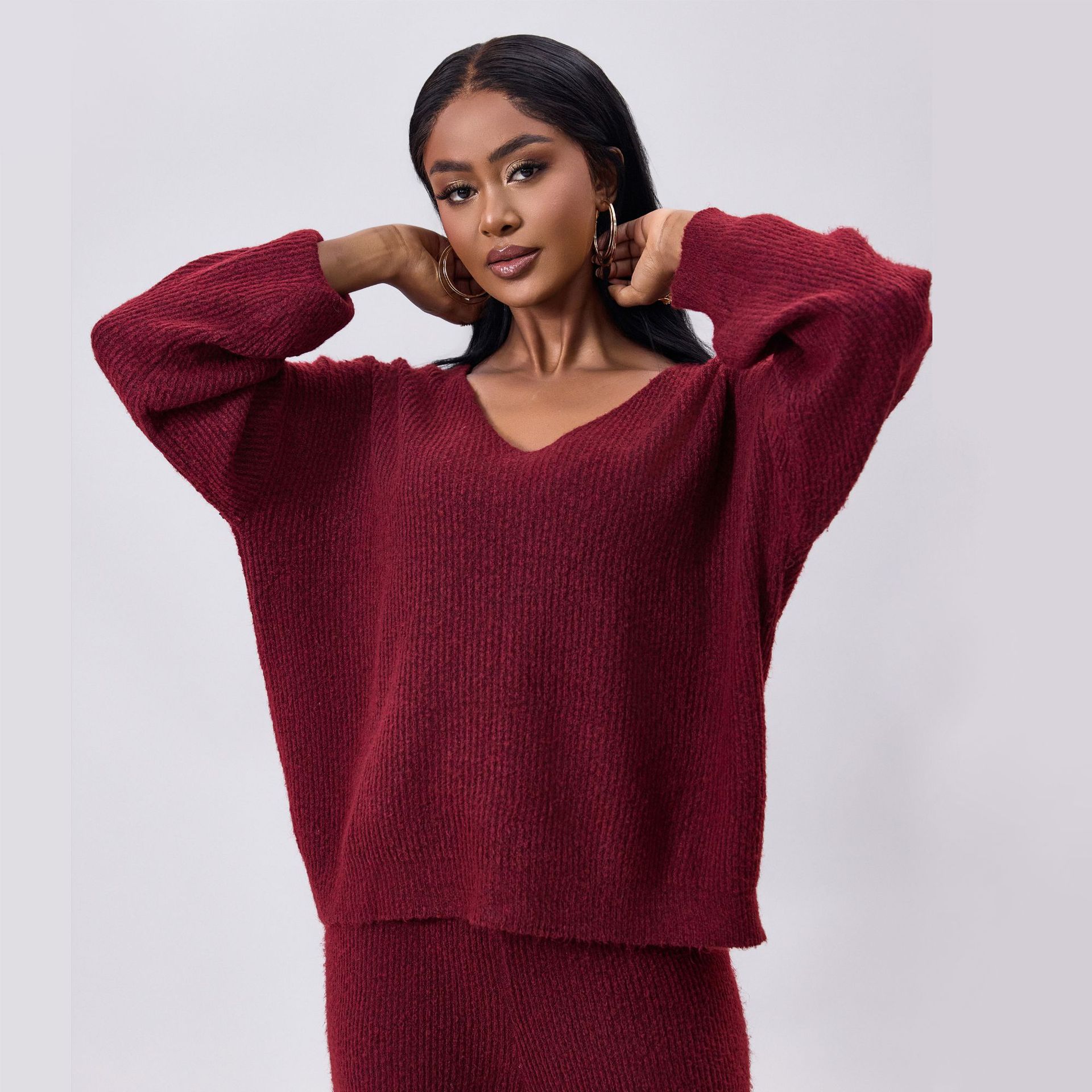 Frau in rotem Strickpullover und passender Hose, modisch und elegant, posiert vor grauem Hintergrund. Herbstmode, Damenbekleidung, Strickwaren.