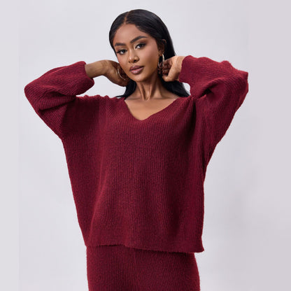 Frau in rotem Strickpullover und passender Hose, modisch und elegant, posiert vor grauem Hintergrund. Herbstmode, Damenbekleidung, Strickwaren.