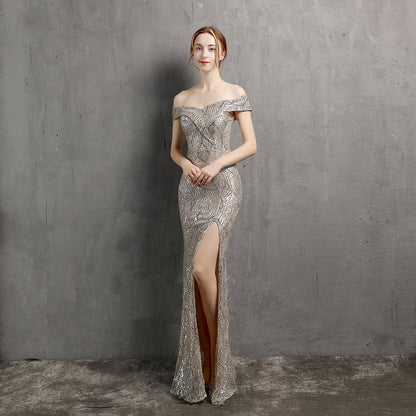 Elegantes Abendkleid mit Pailletten, schulterfreiem Design und hohem Beinschlitz, getragen von einer Frau vor grauer Wand. Perfekt für Gala oder Ball.