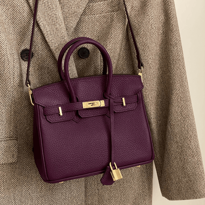 Lila Designer-Handtasche aus Leder mit goldenen Details, hängend an einem beigen Mantel. Luxuriöse Modeaccessoires, stilvoll und elegant.