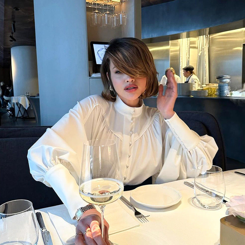 Eine Frau in einem eleganten Restaurant trägt eine weiße Bluse und hält ein Weinglas. Stilvolle Abendessen-Szene, moderne Inneneinrichtung.