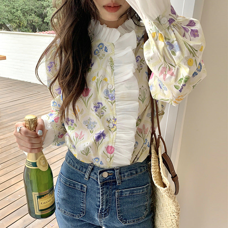 Frau in geblümter Bluse mit Sektflasche, Jeans und Strohtasche auf Holzterrasse. Frühlingsmode, Freizeitlook, stilvolle Damenbekleidung.