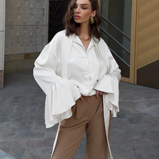 Frau in eleganter weißer Bluse mit weiten Ärmeln und brauner Hose, steht vor moderner Architektur. Modetrend, Damenmode, Streetstyle.