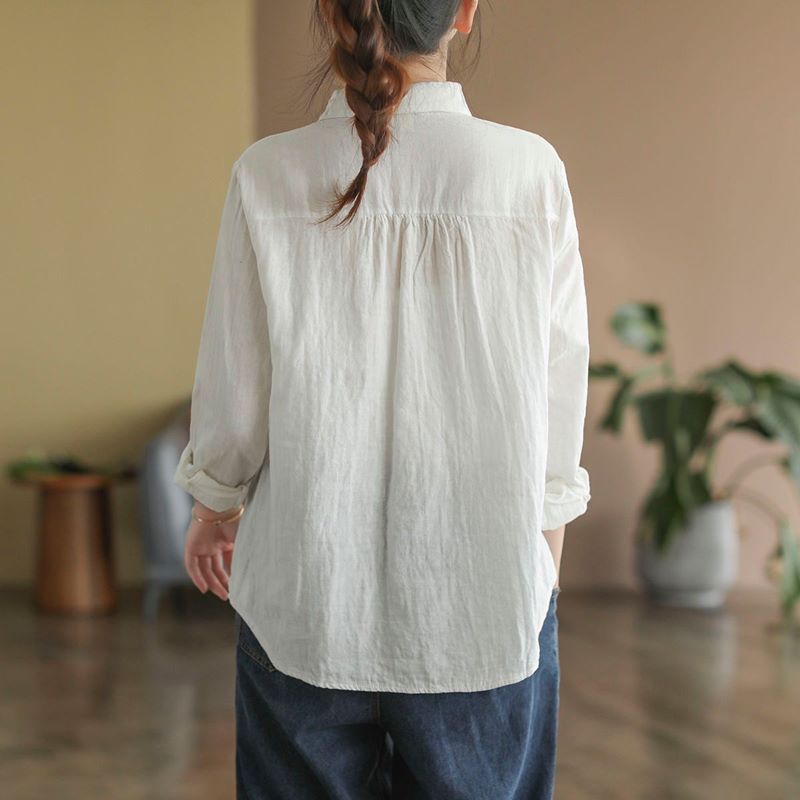 Frau in weißer Bluse und blauer Jeans von hinten, lässiger Stil, Innenraum mit Pflanzen, modische Freizeitkleidung, entspannte Atmosphäre.
