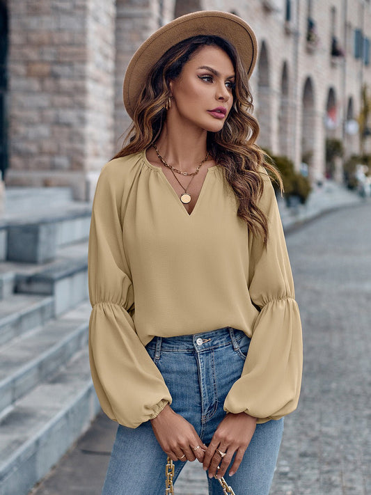 Frau in beiger Bluse und Jeans, trägt Hut und Kette, steht auf gepflasterter Straße vor Backsteingebäude. Modetrend, Streetstyle, Herbstmode.