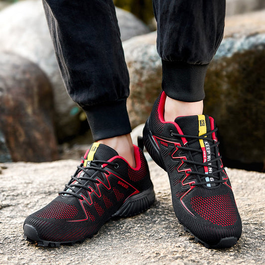 Schwarze und rote Outdoor-Sportschuhe auf steinigem Untergrund, getragen von Person in dunkler Hose. Ideal für Wandern und Trekking.