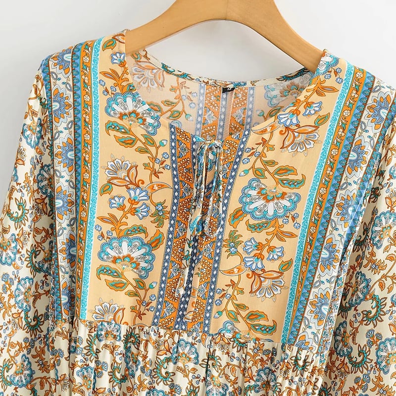 Böhmisches Kleid mit floralen Mustern, langen Ärmeln und Schnürung, in Blau- und Orangetönen auf einem Holzkleiderbügel.