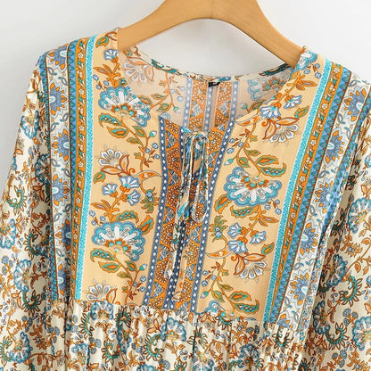 Böhmisches Kleid mit floralen Mustern, langen Ärmeln und Schnürung, in Blau- und Orangetönen auf einem Holzkleiderbügel.