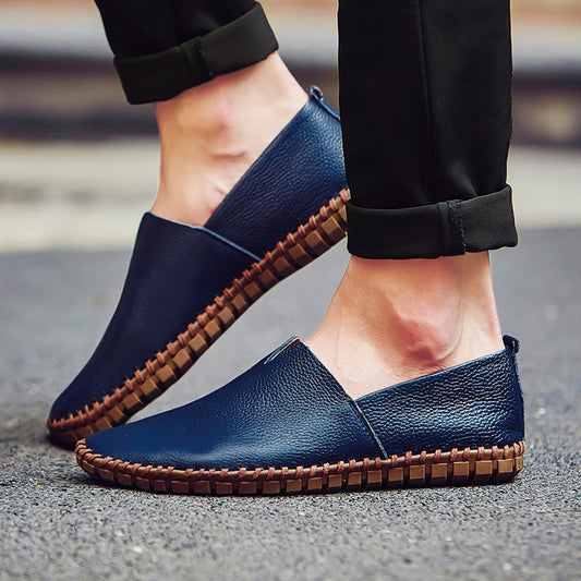 Blaue Herren-Slipper aus Leder mit brauner Sohle auf Asphalt. Modische Freizeitschuhe, ideal für den Alltag. Bequeme und stilvolle Fußbekleidung.