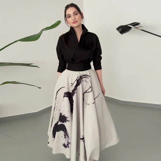 Frau in elegantem schwarz-weißem Kleid mit abstraktem Muster, steht in modernem Raum mit Pflanzen und Designerlampe. Fashion, Mode, Stil.