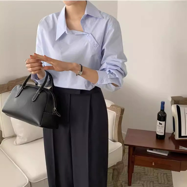 Frau in eleganter, hellblauer Bluse und schwarzer Hose hält schwarze Handtasche. Stilvolle Mode, modernes Outfit, Wohnzimmer.