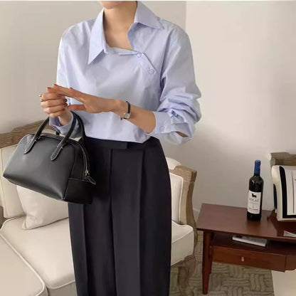 Frau in eleganter, hellblauer Bluse und schwarzer Hose hält schwarze Handtasche. Stilvolle Mode, modernes Outfit, Wohnzimmer.