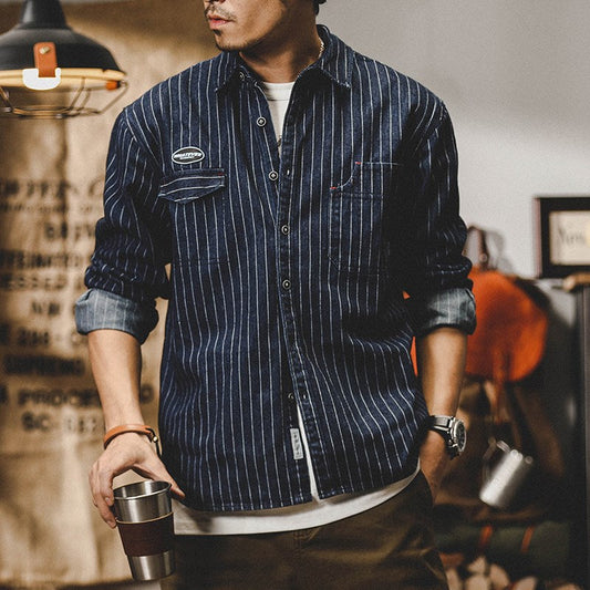 Mann in gestreiftem Jeanshemd, lässiger Stil, hält Thermobecher. Mode für Herren, Freizeitkleidung, urbaner Look.