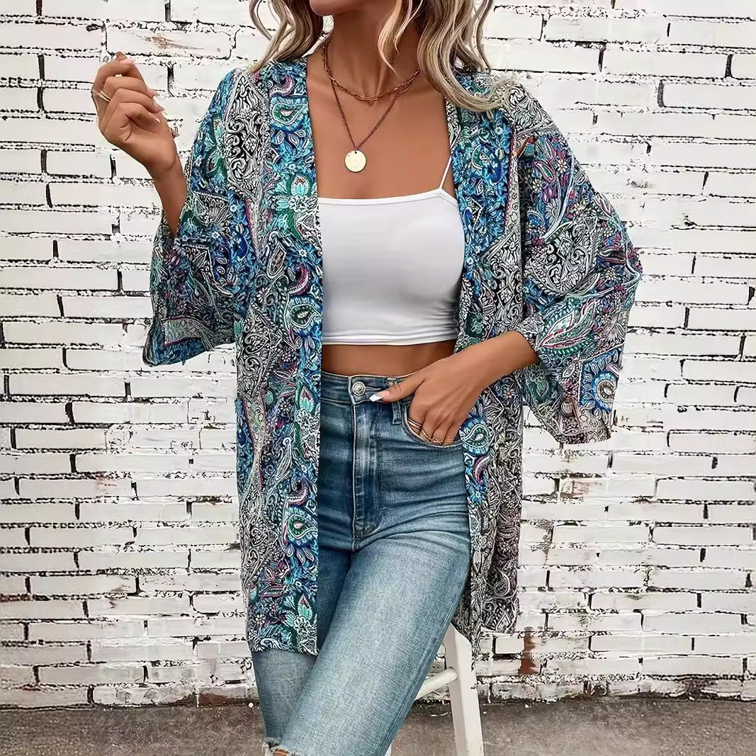 Frau in modischem, blau-gemustertem Kimono, weißem Top und Jeans vor weißer Ziegelwand. Trendige Damenmode, lässiger Boho-Stil.