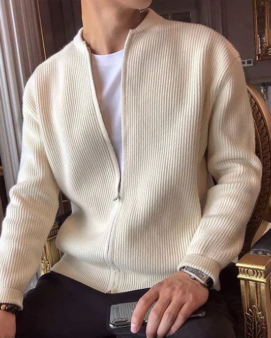Mann trägt cremeweißen Strick-Cardigan mit Reißverschluss, sitzt auf einem Stuhl. Modischer Herrenpullover, eleganter Freizeitlook.