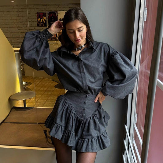 Frau in grauem, voluminösem Kleid mit Rüschen und Knöpfen, steht in modernem Raum. Modetrend, elegantes Outfit, stilvolle Damenmode.