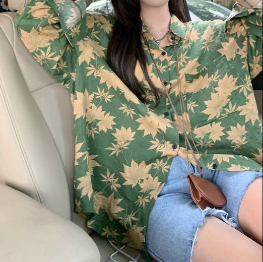 Frau in grünem, blattgemustertem Hemd und blauen Jeansshorts sitzt im Auto. Modetrend, lässiger Stil, Herbstmode, Freizeitkleidung.