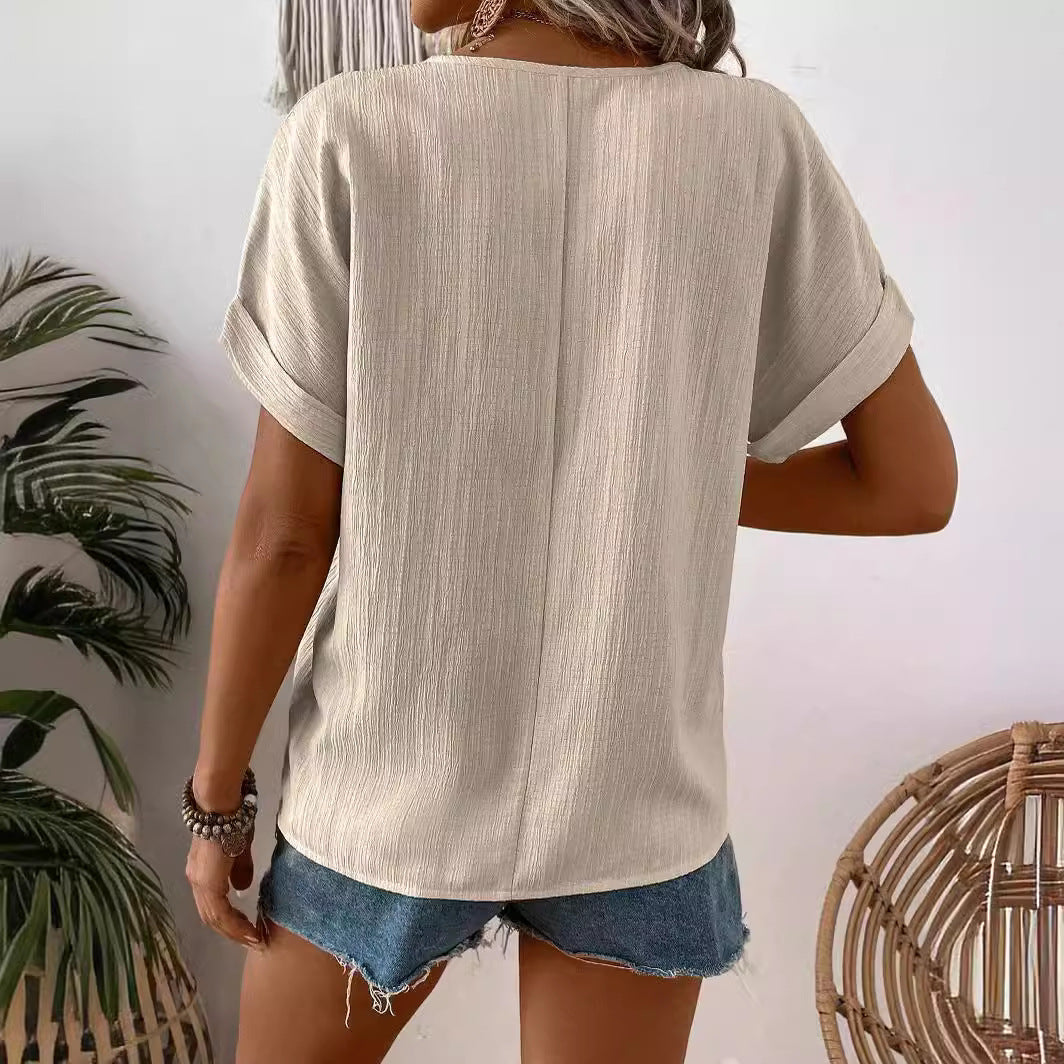 Frau in beigem T-Shirt und blauen Jeansshorts von hinten, umgeben von Pflanzen und Rattanmöbeln, sommerlicher Freizeitlook.