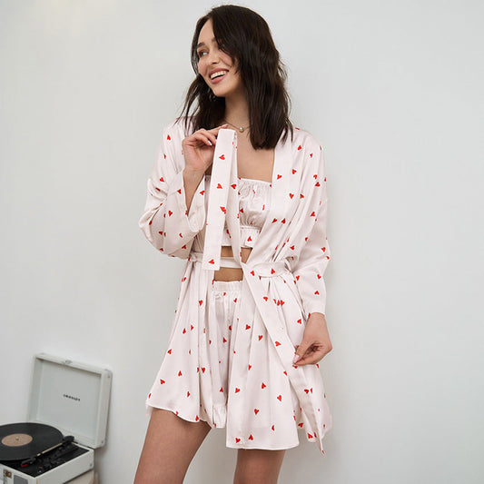 Frau in weißem Pyjama-Set mit roten Herzen, lächelnd, vor einem Plattenspieler. Bequeme Nachtwäsche, modisches Design, entspannte Atmosphäre.