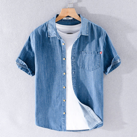 Kurzarm-Jeanshemd für Herren, blau, mit Brusttasche, über weißem T-Shirt, auf Holzbügel. Modisches Herrenhemd, lässiger Stil.