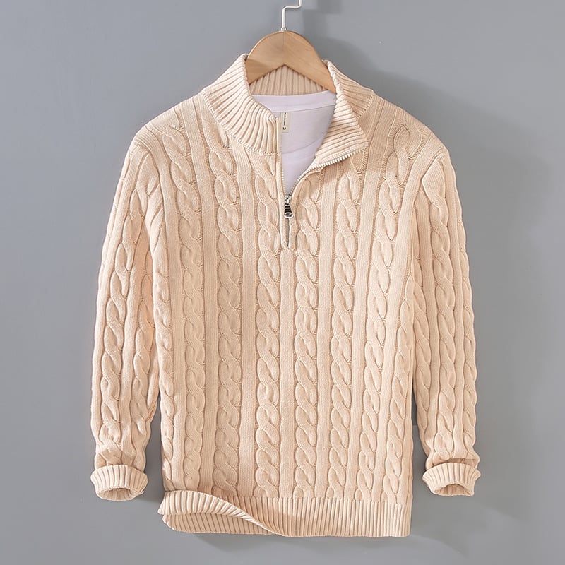 Beiger Strickpullover mit Zopfmuster, Reißverschluss und Stehkragen auf einem Kleiderbügel vor grauem Hintergrund. Modischer Herrenpullover.