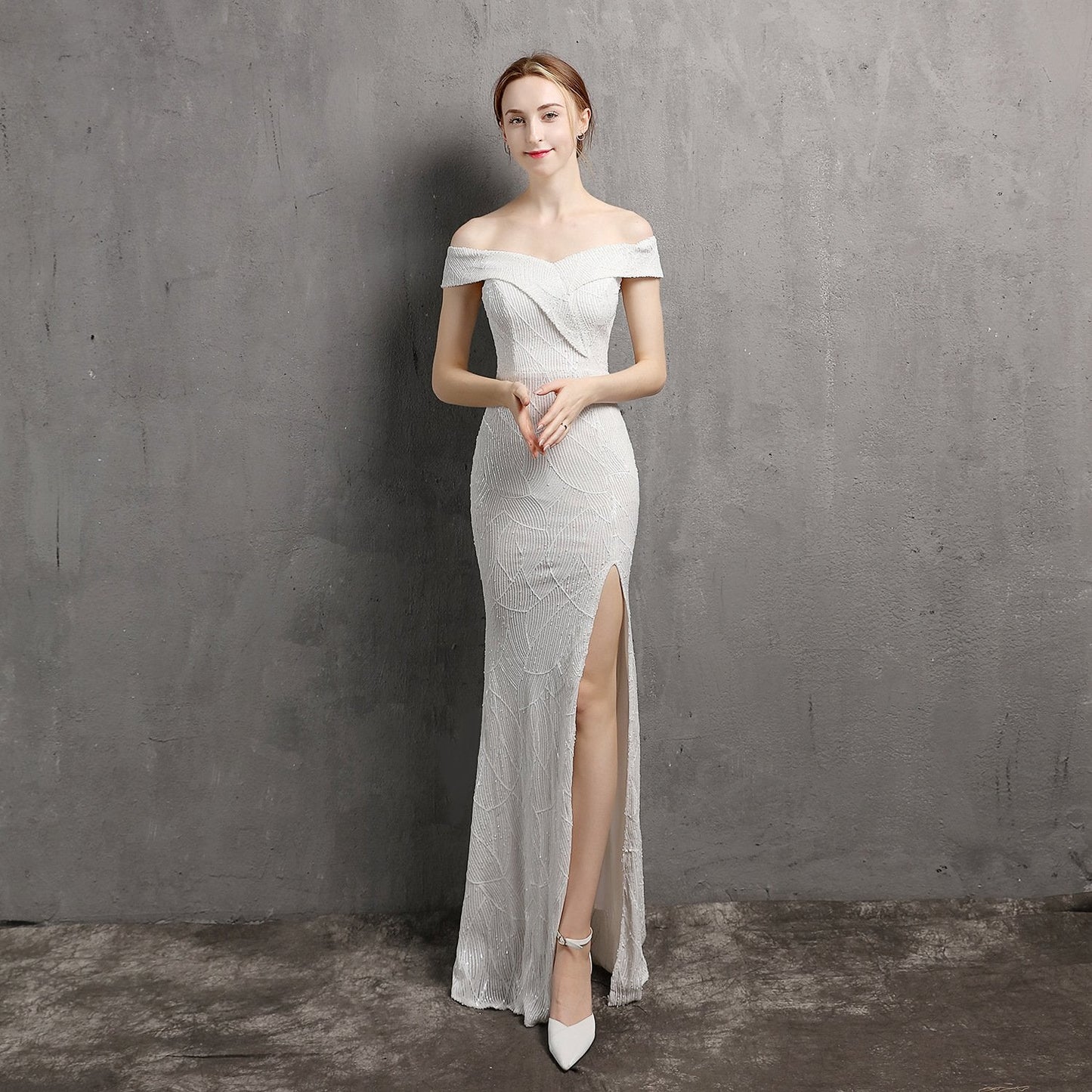 Elegantes Abendkleid in Weiß mit Schulterfrei-Design und hohem Beinschlitz, getragen von einer Frau vor grauem Hintergrund.