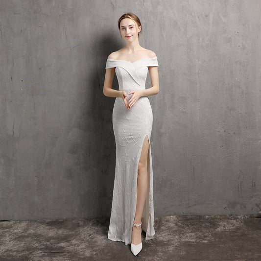 Elegantes Abendkleid in Weiß mit Schulterfrei-Design und hohem Beinschlitz, getragen von einer Frau vor grauem Hintergrund.