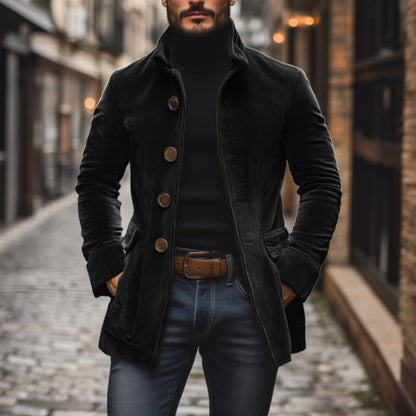 Mann in schwarzem Cordmantel und Rollkragenpullover, steht auf gepflasterter Straße in urbaner Umgebung. Modischer Herbstlook, Herrenmode.