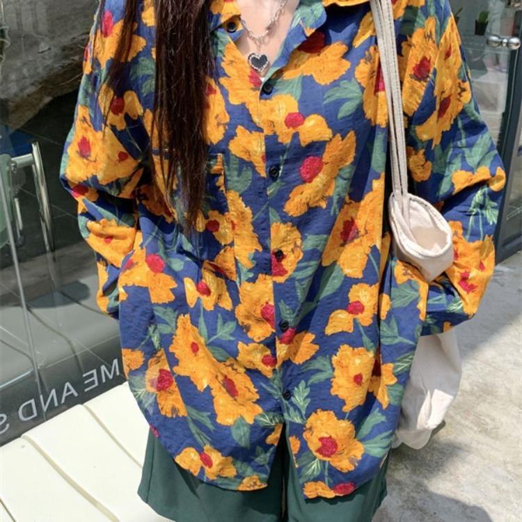 Frau in bunter Blumenbluse mit gelben und roten Blumen, trägt weiße Stofftasche. Modetrend, lässiger Stil, Sommermode, Outdoor.