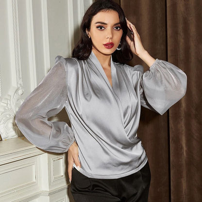 Frau in eleganter, silberner Bluse mit langen Ärmeln, posiert vor einem klassischen, weißen Hintergrund. Mode, Damenbekleidung, stilvoll.