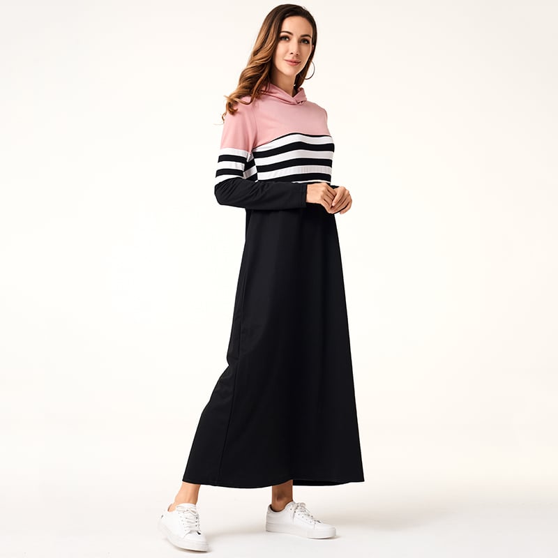 Frau in langem, gestreiftem Hoodie-Kleid in Rosa, Schwarz und Weiß, trägt weiße Sneaker. Modetrend, lässiger Stil, Damenbekleidung.