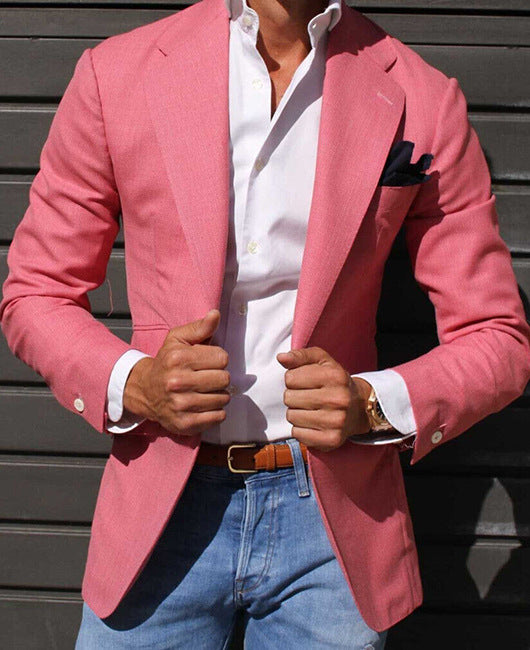 Mann in rosa Sakko, weißem Hemd und blauer Jeans vor grauer Wand. Elegante Herrenmode, stilvoller Look, modisches Outfit.