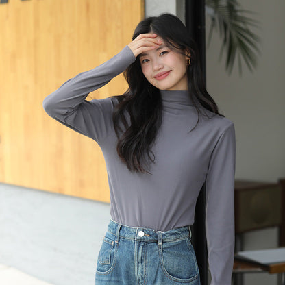 Junge Frau in grauem Rollkragenpullover und blauer Jeans lächelt und steht vor einem modernen Gebäude. Mode, Freizeitkleidung, urbaner Stil.