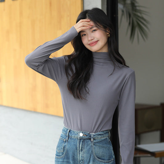 Junge Frau in grauem Rollkragenpullover und blauer Jeans lächelt und steht vor einem modernen Gebäude. Mode, Freizeitkleidung, urbaner Stil.
