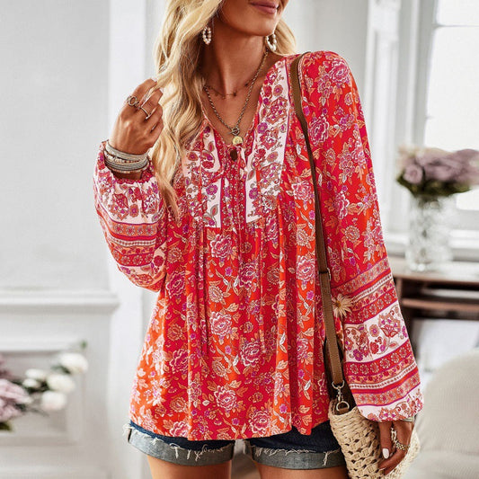 Frau in roter, geblümter Bluse mit langen Ärmeln und Jeansshorts, steht in modernem, hellen Raum. Boho-Stil, modische Sommerkleidung, Freizeitlook.