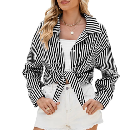 Frau trägt schwarz-weiß gestreifte Bluse, geknotet, mit weißem Top und weißen Shorts. Modetrend, Sommeroutfit, lässiger Stil.
